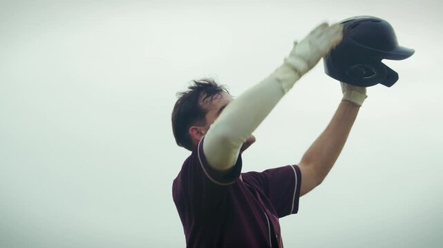 Baseball player in uniform celebrates a hard-earned victory. He raises his helmet high and acknowledges the crowd with a kiss to his glove, showing immense joy.