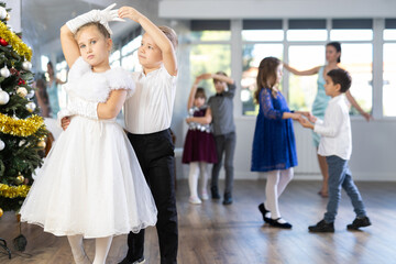 Obraz premium Positive elementary students in festive attire rehearsing ballroom dance number for upcoming Christmas party at school with interested female teacher in background..