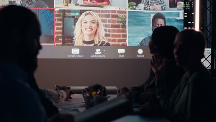 Multiethnic group attends a digital meeting from office at night, communicating with the main investor and international associates to align planning, finance and corporate objectives. Camera B.