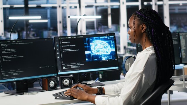 Data center female programmer using machine learning algorithms to analyze datasets. African american woman in server farm using AI neural networks to recognize data patterns, camera A