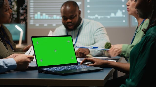 Diverse project staff working at night in office with chroma key on laptop, collaborating on reporting and setting business goals during a night time meeting in a corporation space. Camera B. - Powered by Adobe