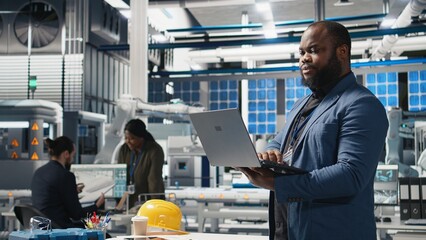 African american director in a solar panels facility monitoring performance and efficiency metrics, combining leadership with real time quality control and strategic business development. Camera A.