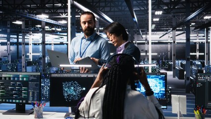 Team of engineers doing brainstorming in server room using AI to review infrastructure diagnostics. Teamworking IT colleagues in data center analyzing data using artificial intelligence, camera A
