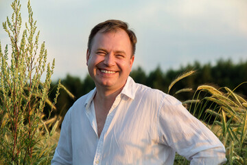 Man in white shirt standing in rye field at sunset.