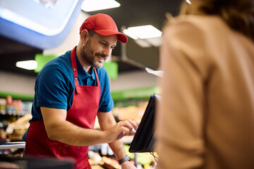 Smiling cashier working at supermarket checkout.