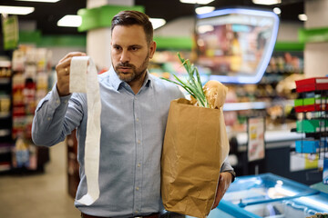 Worried man looking at bill after buying groceries at supermarket.