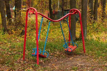 A children's metal swing was damaged by a fallen tree in a forest or city garden. Iron pipes on the playground were bent after the elements and storm winds