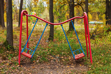 A children's metal swing is damaged, and the iron pipe is bent by a fallen tree. An abandoned playground and old amusement park in the woods