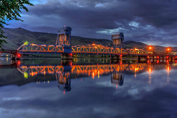 Night photo of blue draw bridge spanning the Snake River connecting Lewiston ID and Clarkston WA with the bridge and colorful lights reflecting the the water