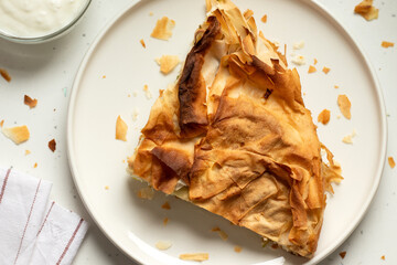 Homemade burek slice with yogurt on a kitchen table. Top view.