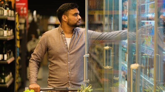 Young Indian man choosing a cold drink at the grocery store
