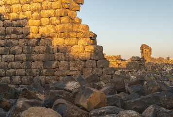 Umm Al-Jimal Sunset: Golden hour on the ancient black basalt ruins in Mafraq, Jordan. Roman tower contrasts with modern cell towers.