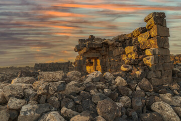 Umm Al-Jimal Sunset: Golden hour on the ancient black basalt ruins in Mafraq, Jordan. Roman tower contrasts with modern cell towers.