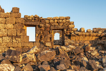 Umm Al-Jimal Sunset: Golden hour on the ancient black basalt ruins in Mafraq, Jordan. Roman tower contrasts with modern cell towers.