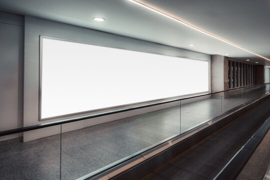 Large bright mock-up billboard beside an airport-style travelator in a clean modern corridor, illuminated by soft ceiling lights and offering spacious template space for advert design; banner template