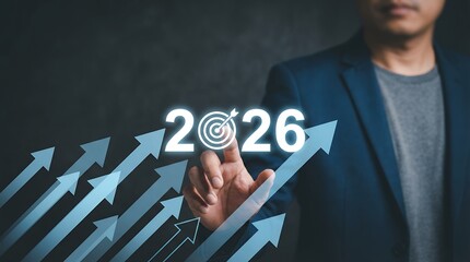 A businessman's finger touches the year 2026 displayed with a target symbol set against a backdrop of upward pointing blue arrows representing growth and progress success future strategy