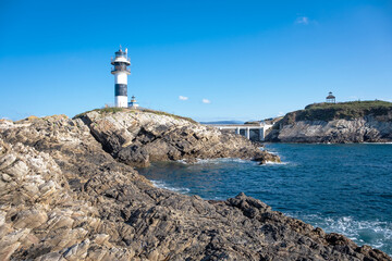 black and white lighthouse standing on a rocky cliff by the deep blue sea under a clear sky, Isla de Pancha, Ribadeo, Galicia, Spain