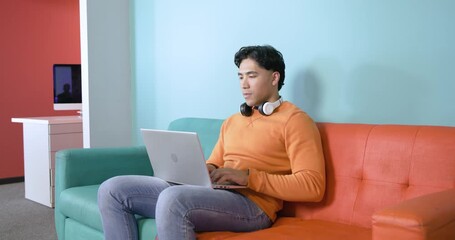 Asian man starting laptop in home office pressing button, watching screen, smiling, typing tasks