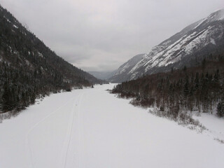 Naklejka premium Aerial view of the glacial valley at the bottom of which lies a frozen river covered with snowmobile tracks
