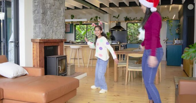 After stepping into living area near stone fireplace mom guiding Indian girl in holiday dancing