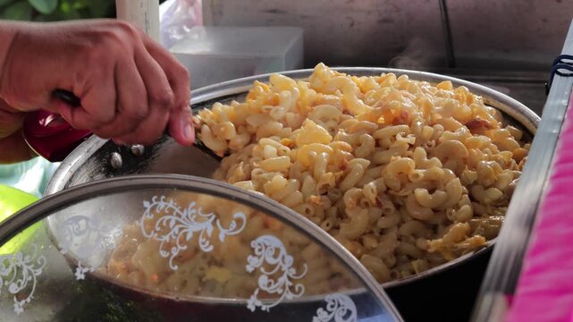 Close-up view of street vendor stirring creamy macaroni and cheese in a large metal pot