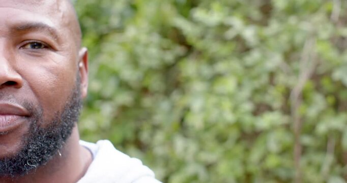 African American male getting camera prompt, shifting smirk into laugh in garden shrubs, copy space