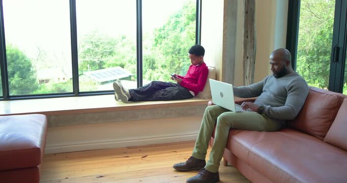 African American father and son pausing typing and tapping smartphone exchanging feedback at home