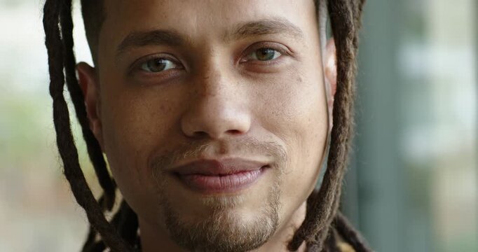 Dreadlocked mid adult man shifting from serious face into broad grin in front of window pane