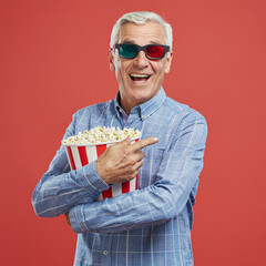 Excited senior man watching d movie with d glasses and popcorn in d cinema theater hall