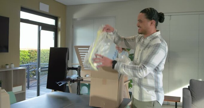 Mid adult man entering lounge carrying box, unwrapping bubble wrap and revealing gold lamp base