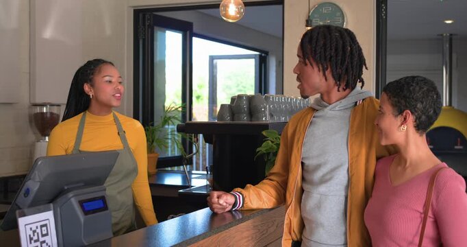 Man pointing at menu board, couple leaning in coffee shop, barista explaining options steaming milk