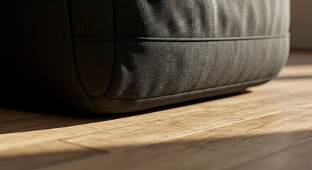 Close-up of a dark gray beanbag on a light brown wooden floor, illuminated by sunlight.
