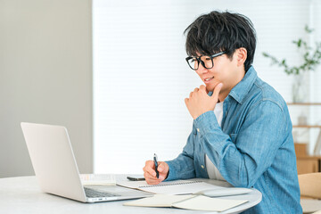 Serious young Asian man studying at home (university student, graduation thesis, report, paper)
