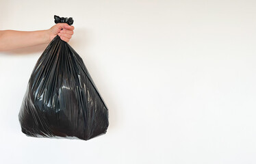 A maid's hand holds a full black garbage bag at arm's length against a white wall. Space for text, advertising