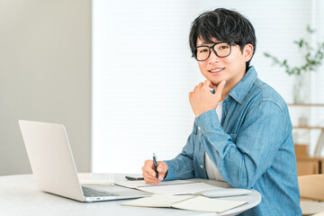 家でスキルアップのために勉強する真面目な若いアジア人男性（自己投資,マネジメント,自宅学習）  © buritora