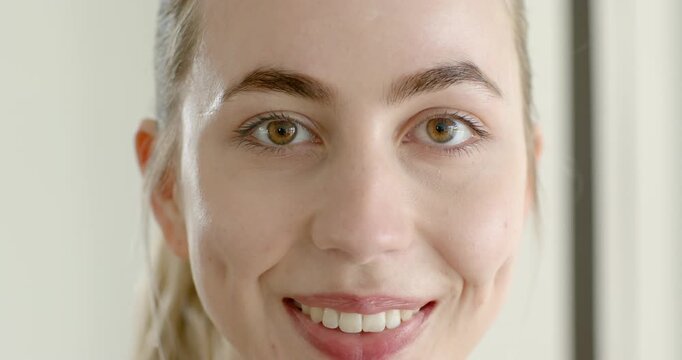 Female maintaining calm face and smiling before deepening grin and showing dimples in pale room
