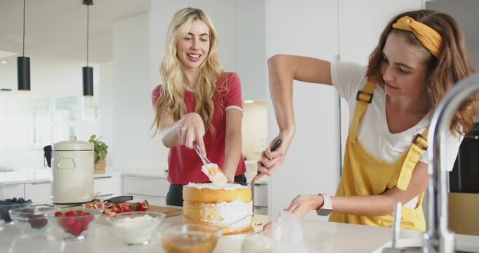 Spotting cake on turntable, friends smoothing frosting with spatulas rotating laughing on island
