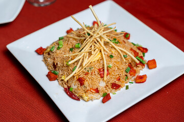 Peruvian chaufa rice dish with vegetables and crispy garnish, served on a white plate and styled with vibrant colors and appetizing presentation.