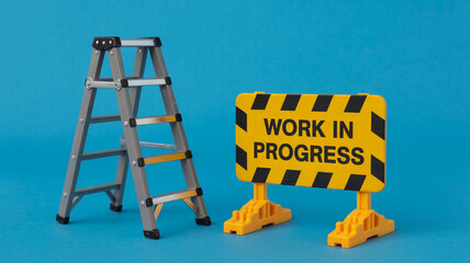 Miniature step ladder and 'Work in Progress' sign on solid turquoise background representing ongoing project
