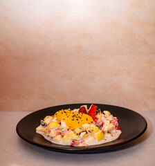 Plato negro con ensalada dulce de frutas con crema estilo navideño en fondo de marfil color crema