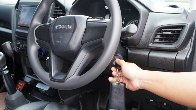 Wonosobo, Indonesia - 19 November 2025: Hand holding a car key near an Isuzu steering wheel inside the vehicle's modern dashboard interior.