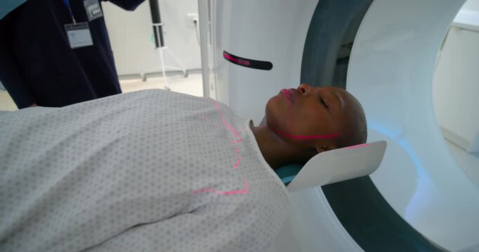 CT tech in hijab adjusting panel after red lasers while African American woman lying for scan