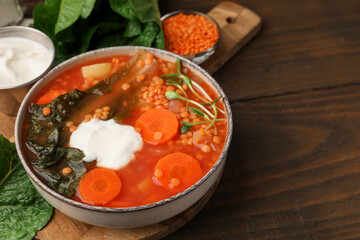 Tasty lentil soup with sour cream in bowl on wooden table, closeup. Space for text