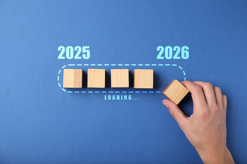 New Year 2026. Man putting wooden cube next to others onto loading bar on blue background, top view