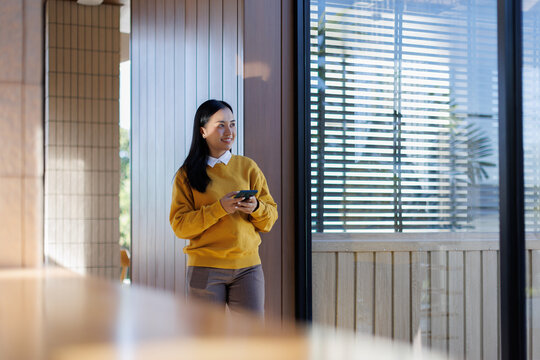A woman wearing a yellow shirt is using her phone in the office. - Powered by Adobe