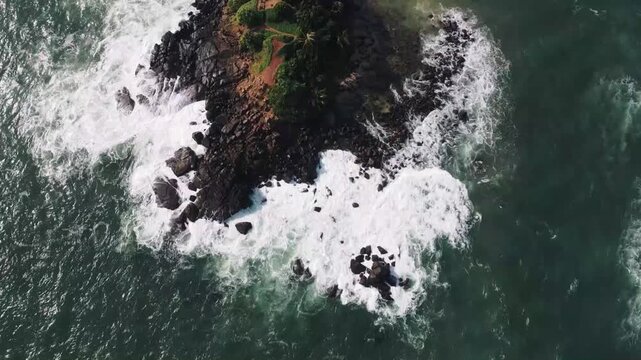 Aerial view of ocean waves pounding rocky shoreline on the Parrot Rock, showcasing Mirissa beach landscape in southern Sri Lanka