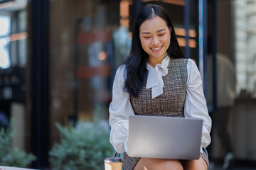Image of a woman working on her laptop computer at an outdoors table, typing on the laptop keyboard, working remotely.
