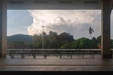 Scenic view from a train station platform with tropical trees, palm trees, and cloudy skies during golden hour