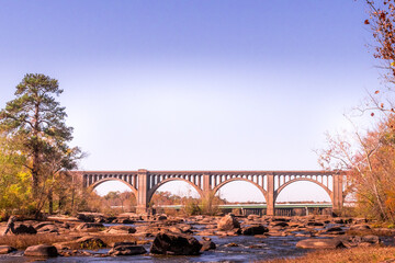 The beautiful arches of the  CSX-A line bridge over the James River in Richmond Virginia on an Autumn day with trees, rocks, and rapids