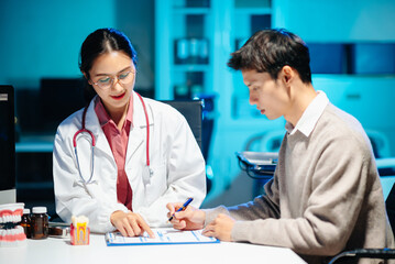Fototapeta premium Asian female dentist explains dental model and treatment form to patient during consultation